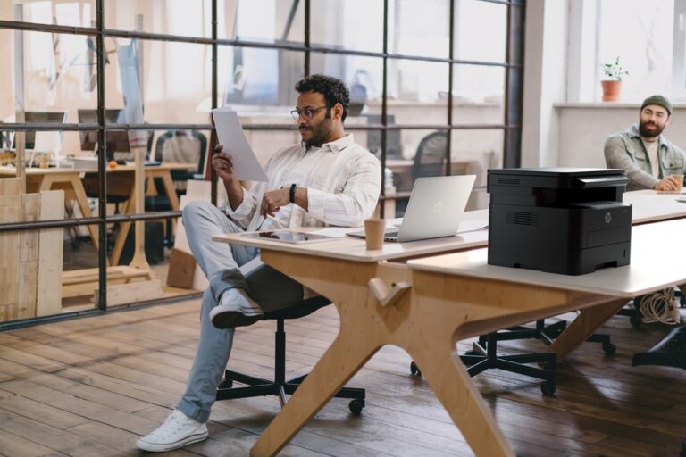 Focused man reading papers in office near colleague with laptop tablet and computer