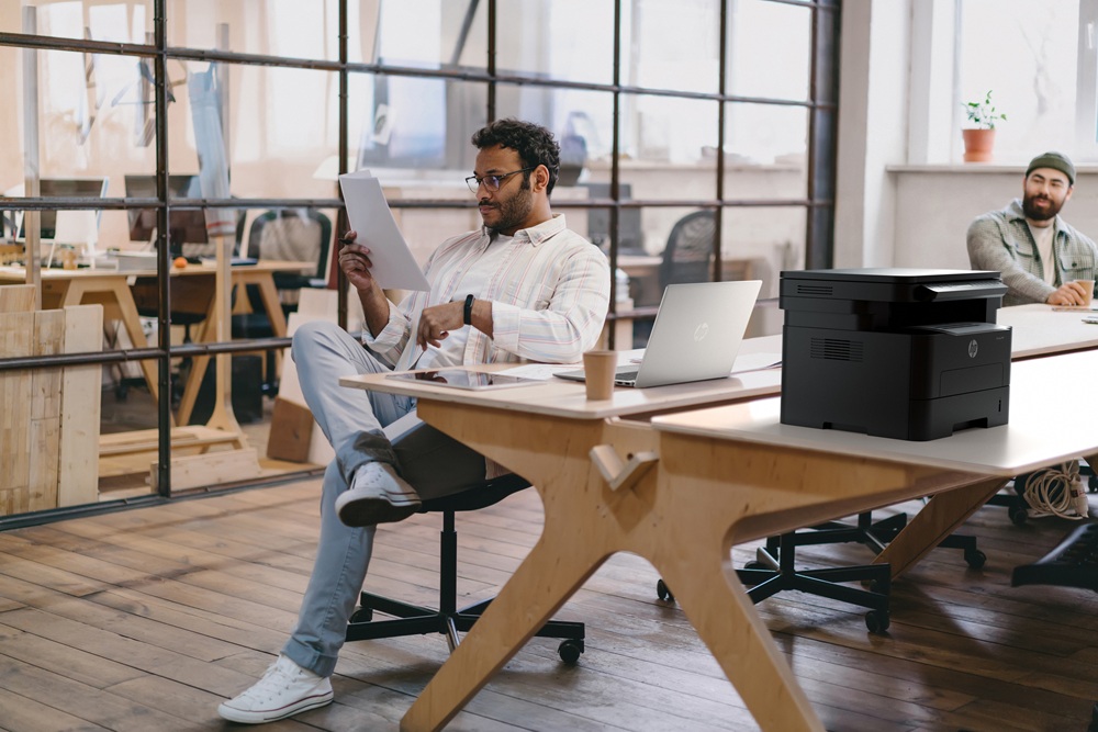 Focused man reading papers in office near colleague with laptop tablet and computer